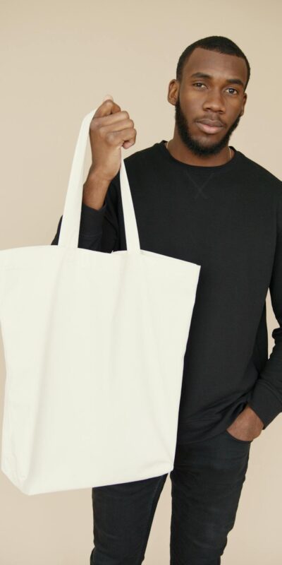 Portrait of a young man holding a blank white tote bag, ideal for mockup and branding purposes.